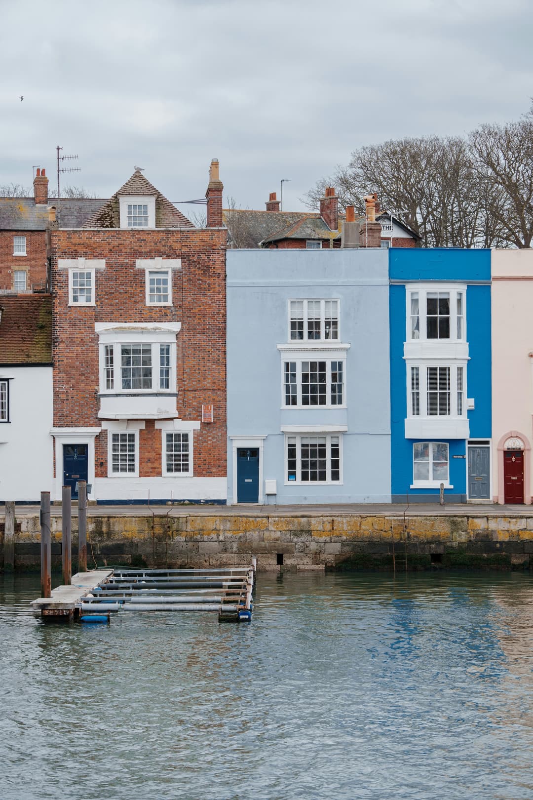 Blue and brick townhouses standing along a Sussex quayside above still water