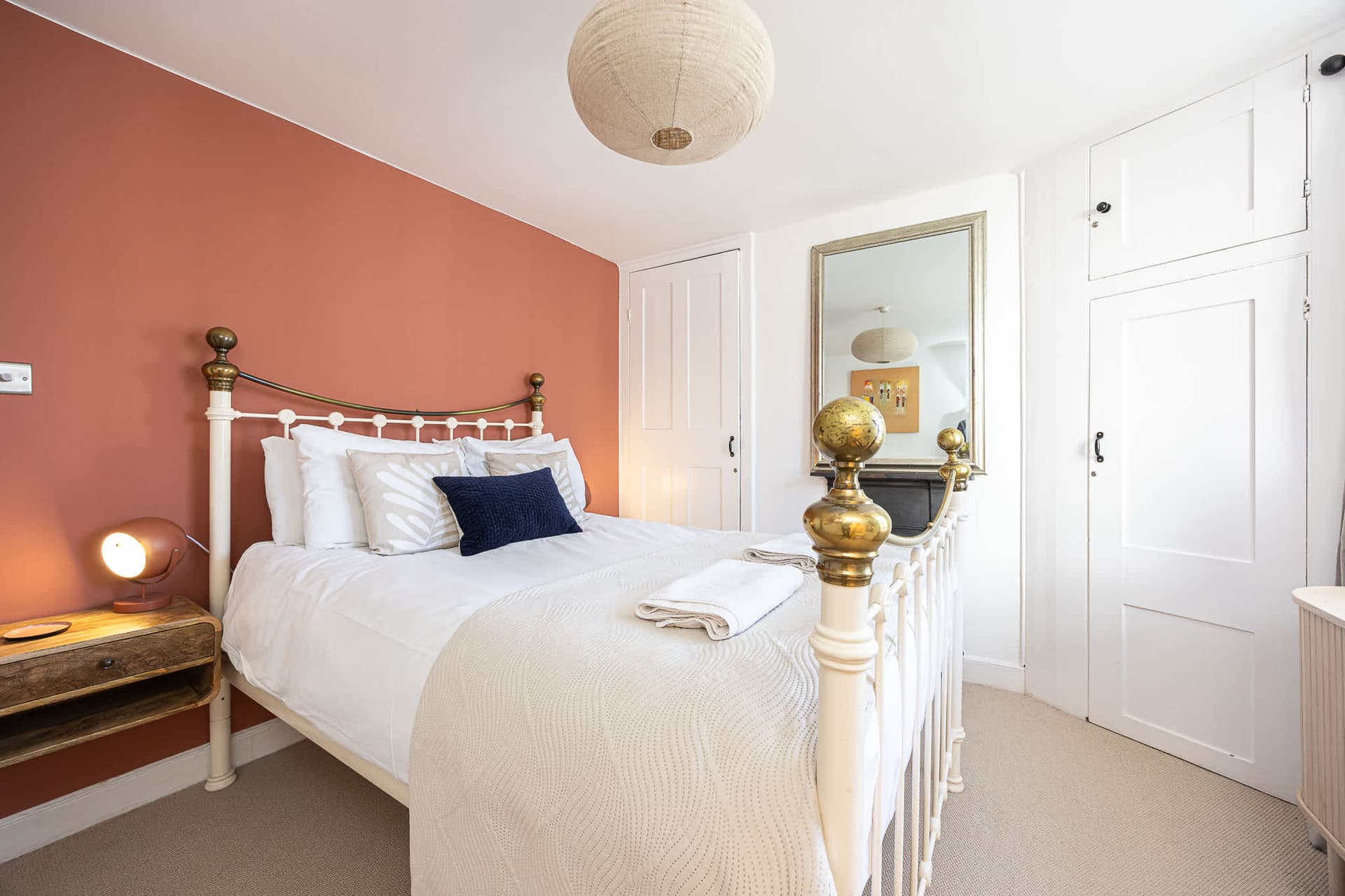 Terracotta bedroom with a brass bed and crisp white linen at a South House Brighton cottage