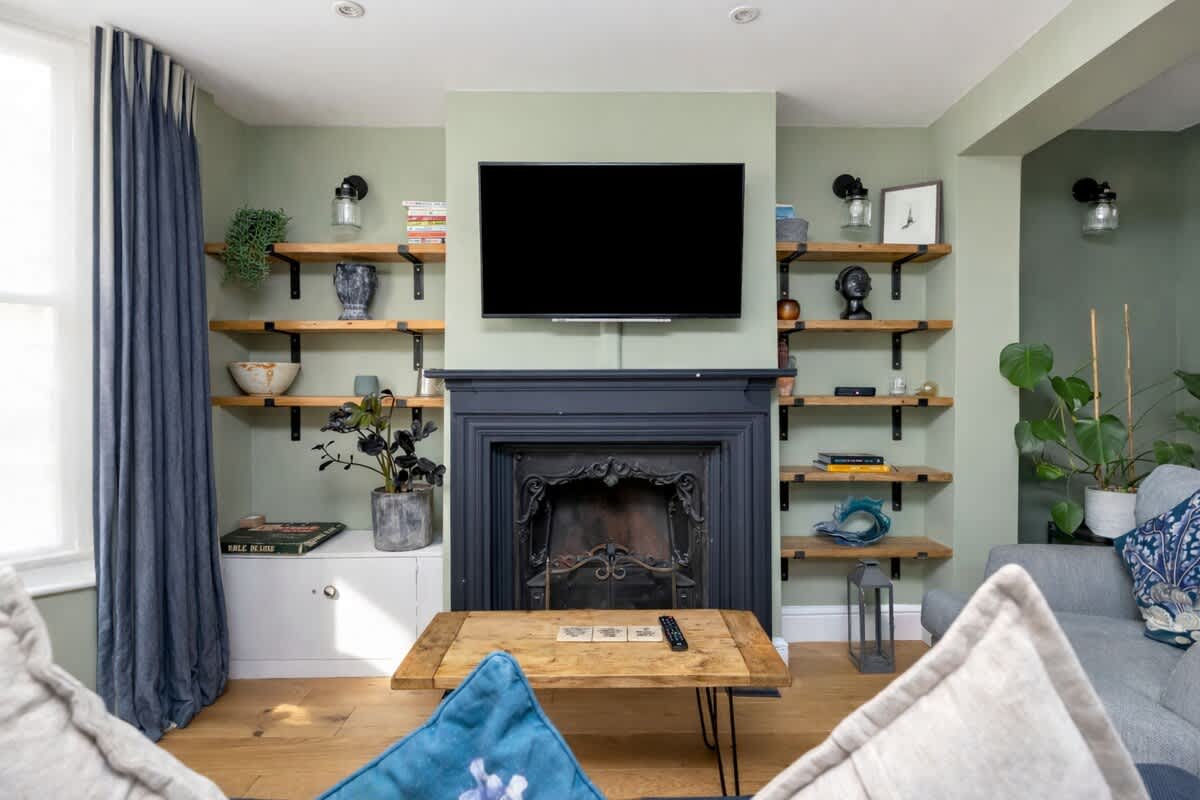 Sage green living room with a black period fireplace and styled open shelving