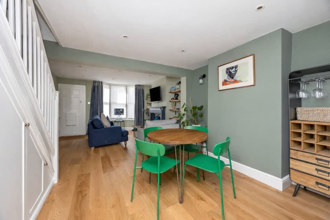 Calm green dining space with bright chairs, artwork and warm wooden floors