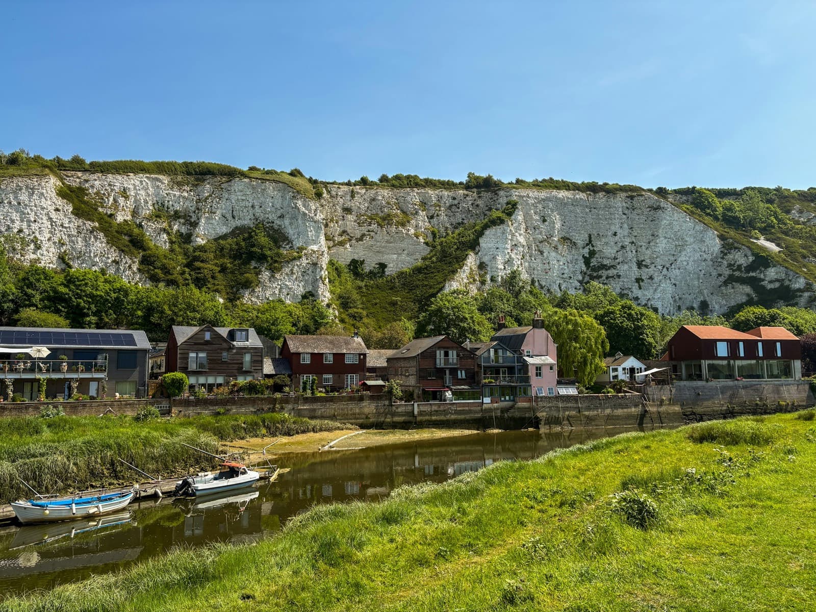 A Sussex village of white houses beneath chalk cliffs, a river running past green banks